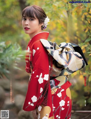 A woman in a red kimono standing in front of a tree.
