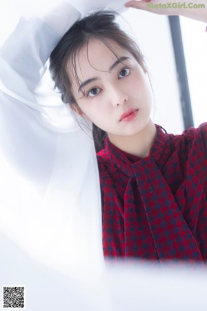 A woman in a red and black plaid dress standing in front of a white wall.