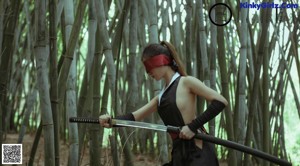 A naked woman with a blindfold standing in a bamboo forest.