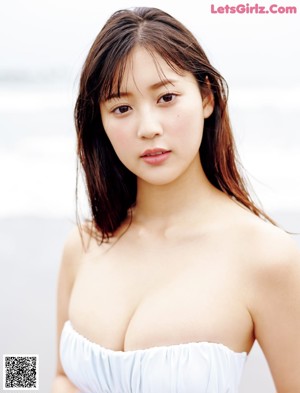 A woman in a white bikini sitting on a bed next to the ocean.