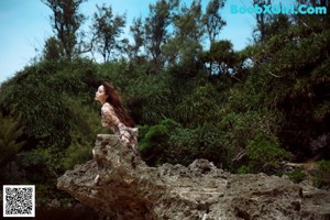 A woman standing on top of a rock next to a cliff.