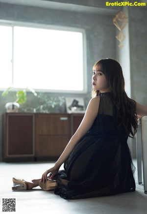 A woman in a gray dress sitting on a bed.