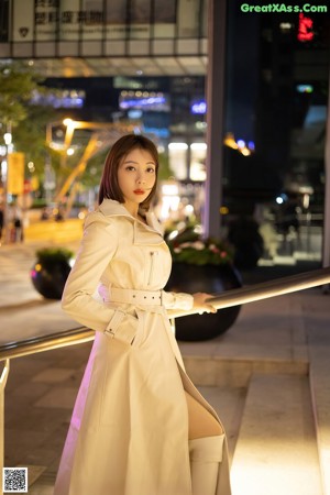 A woman in a trench coat and high heels walking down a hallway.