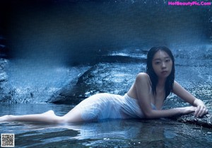 A woman in a white dress standing in front of a waterfall.