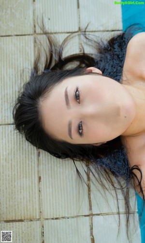 A woman in a bikini leaning against a wall by a pool.