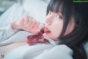 A woman in a school uniform is sitting on a bed.