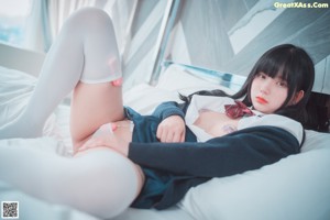 A woman in a school uniform is sitting on a bed.