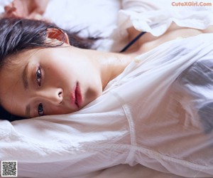 A woman laying on a bed in a white shirt.