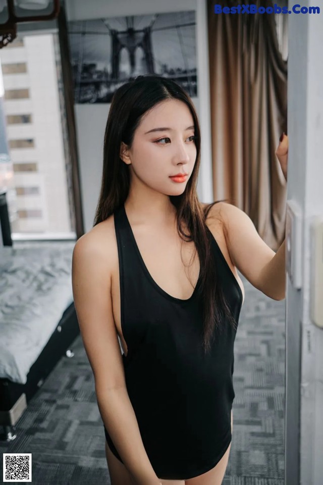 A woman in a black bathing suit leaning against a wall.