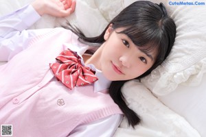 A young woman in a pink sweater and plaid skirt posing on a bed.