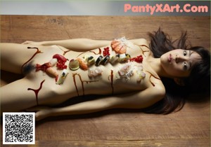 A naked woman laying on a wooden floor covered in sushi.